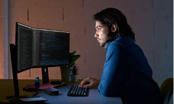 A man is looking at a monitor with his fingers on a keyboard